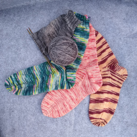 A collection of hand-knitted socks in various colors and patterns, including striped and solid colors, displayed on a textured background.