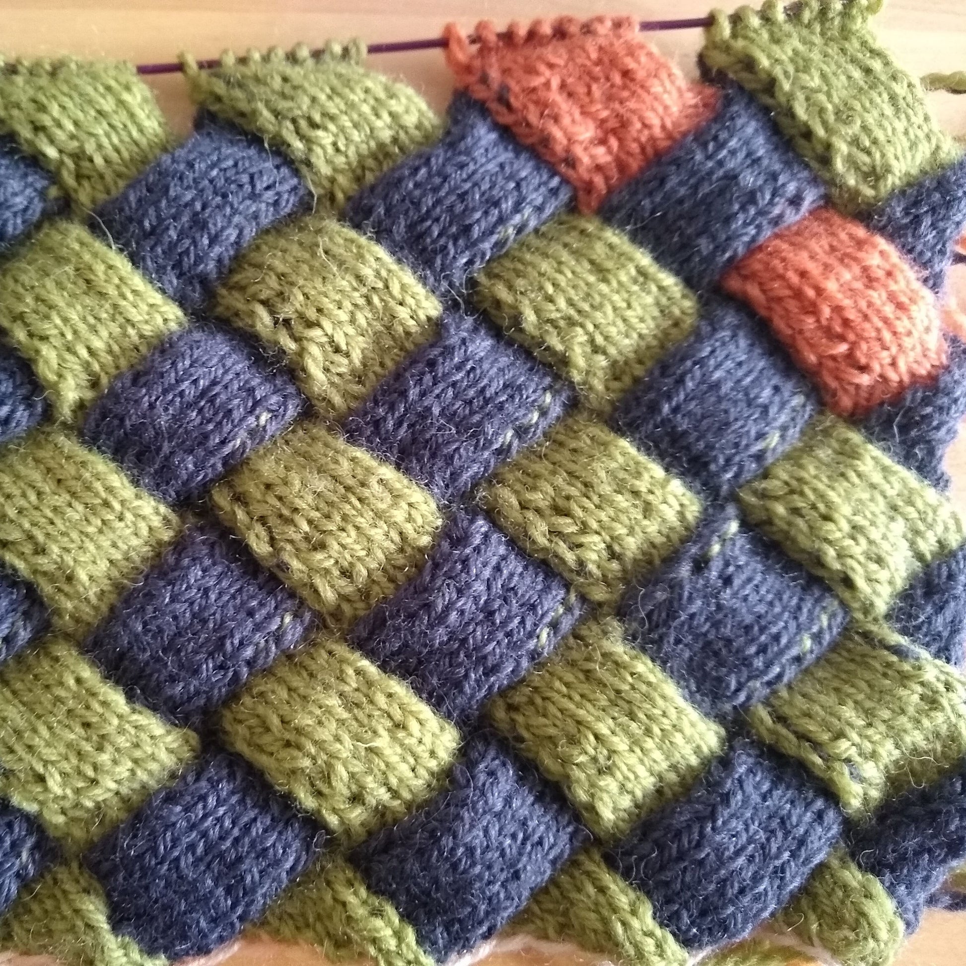 A close-up of a knitted fabric with a geometric pattern featuring green, blue, and orange colors.